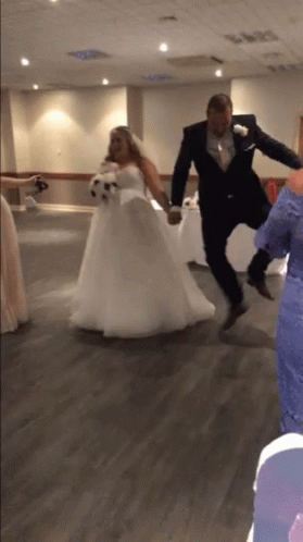 A Bride And Groom Are Jumping In The Air Holding Hands GIF