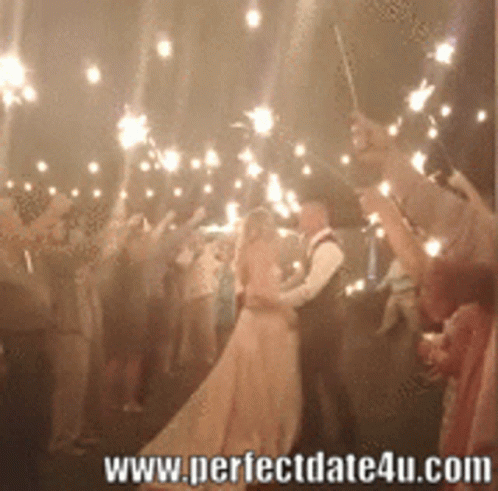 A Bride And Groom Are Kissing Under Sparklers At A Wedding GIF