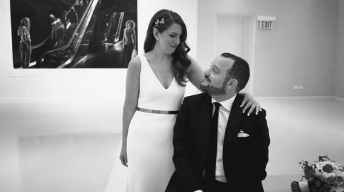 A Bride And Groom Are Posing For A Picture In Front Of An Exit Sign . GIF