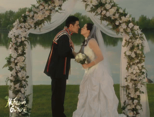 A Bride And Groom Kiss Under A Floral Arch With The Words Mother Gino 'S On The Bottom GIF