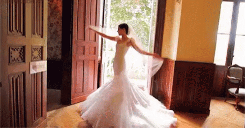 A Bride In A Wedding Dress And Veil Is Dancing In A Room . GIF