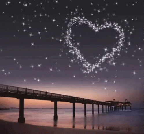 A Bridge Over A Body Of Water With A Heart Made Of Stars In The Sky GIF