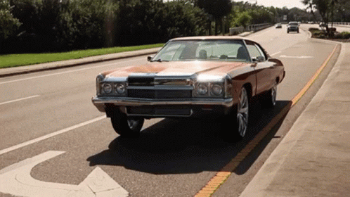 A Brown Car Is Driving Down A Street With A Handicap Sign On The Sidewalk GIF