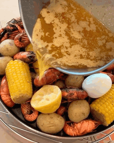 A Bucket Filled With Shrimp Corn Potatoes And Lemons Is Being Poured With Sauce GIF