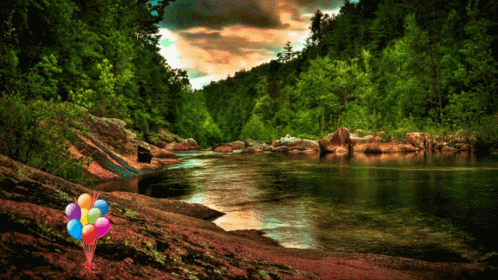 A Bunch Of Balloons Are Sitting On A Rock Near A River GIF