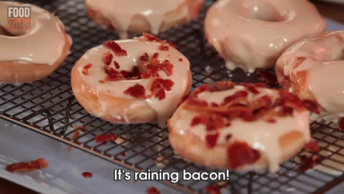 A Bunch Of Donuts Are Sitting On A Cooling Rack With The Words It 'S Raining Bacon GIF