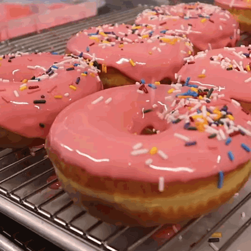 A Bunch Of Donuts With Pink Frosting And Sprinkles On A Rack GIF