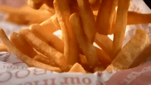 A Bunch Of French Fries Are Being Poured Out Of A Container GIF