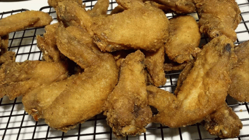 A Bunch Of Fried Chicken Wings Are Sitting On A Wire Rack GIF