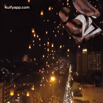A Bunch Of Lanterns Are Flying In The Night Sky Over A City . GIF