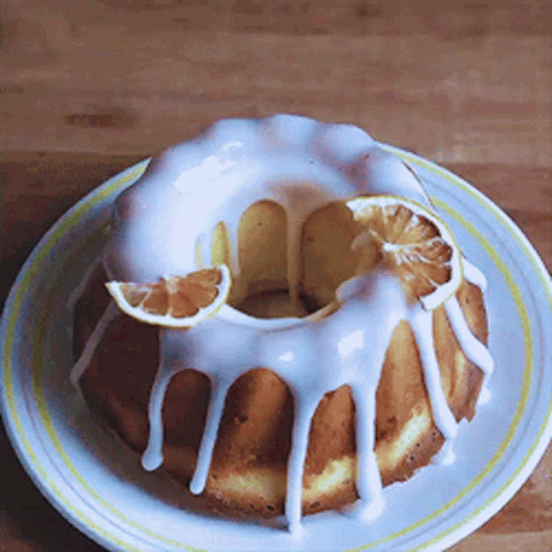 A Bundt Cake With White Frosting And Slices Of Orange On A White Plate GIF