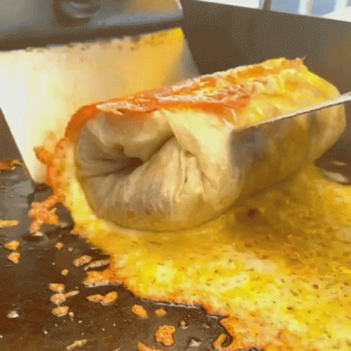 A Burrito Is Being Cut In Half On A Stove Top GIF