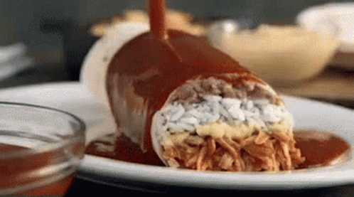 A Burrito On A Plate With Sauce Being Poured On It . GIF