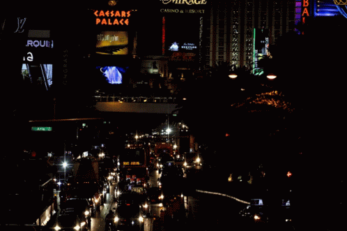 A Busy City Street At Night With A Sign For The Caesars Palace In The Background GIF