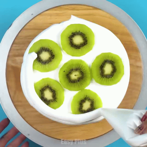 A Cake With Kiwi Slices And Whipped Cream Is Being Decorated By Easy Plus GIF