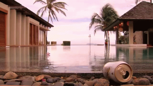A Can Of Beer Is Laying On The Edge Of A Pool GIF