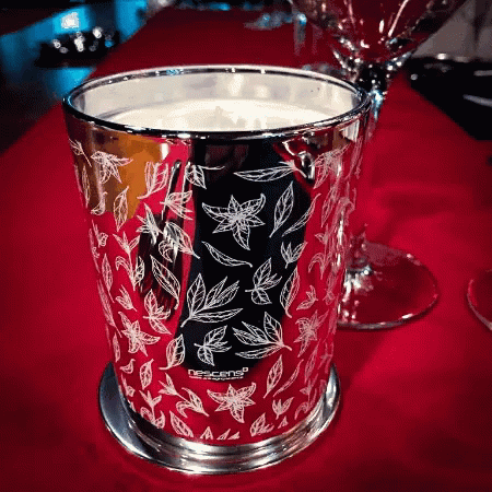 A Candle In A Silver Cup With Leaves On It Is On A Red Table GIF