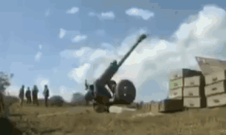 A Cannon Is Being Fired In A Field With Boxes In The Background . GIF