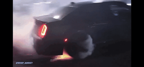 A Car Is Doing A Burnout In The Dark With Smoke Coming Out Of The Tire GIF
