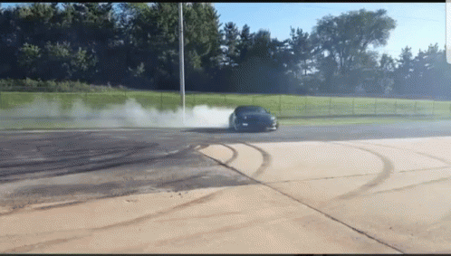 A Car Is Drifting In A Parking Lot With Smoke Coming Out Of The Tire GIF