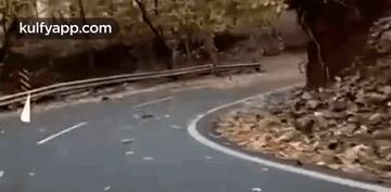 A Car Is Driving Down A Curvy Road With Trees On The Side . GIF