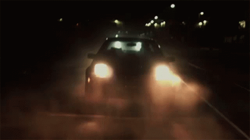 A Car Is Driving Down A Dark Road At Night With Its Headlights On . GIF