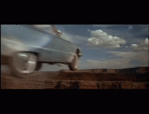 A Car Is Driving Down A Dirt Road With Clouds In The Background GIF