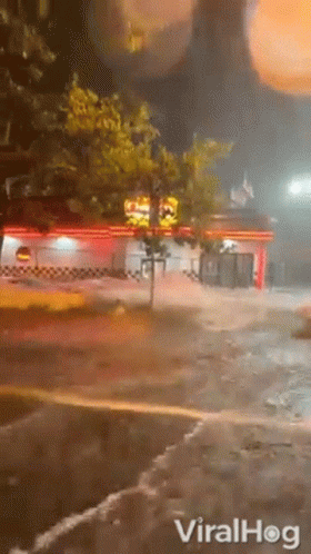 A Car Is Driving Down A Flooded Street At Night In Front Of A Restaurant . GIF