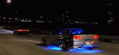 A Car Is Driving Down A Highway At Night And Has Blue Lights On The Tires GIF