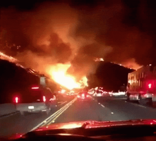 A Car Is Driving Down A Highway In Front Of A Huge Fire GIF
