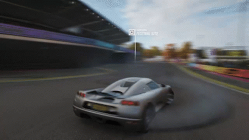 A Car Is Driving Down A Road In Front Of A Festival Site GIF