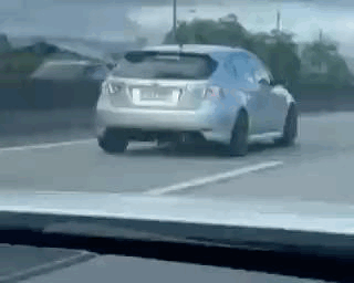 A Car Is Driving Down A Road Next To A Parking Lot . GIF