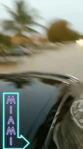 A Car Is Driving Down A Road With A Neon Sign Pointing To Miami GIF