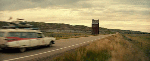 A Car Is Driving Down A Road With A Sign In The Background That Says ' Ghostbusters ' GIF