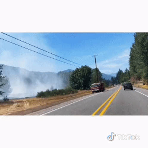 A Car Is Driving Down A Road With Smoke Coming Out Of The Mountains Behind It GIF