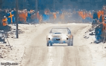 A Car Is Driving Down A Snow Covered Road In Front Of A Crowd . GIF