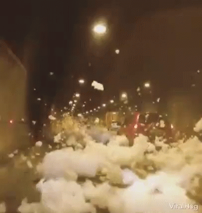 a car is driving down a snowy street at night with a lot of snow on the ground .