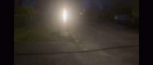 A Car Is Driving Down A Street At Night With A Bright Light Shining Through The Fog GIF