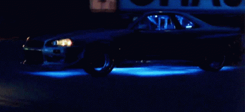 A Car Is Driving Down A Street At Night With Blue Lights On The Wheels GIF