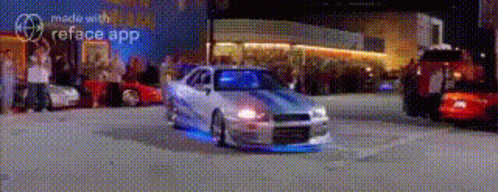 A Car Is Driving Down A Street In Front Of A Crowd Of People . GIF