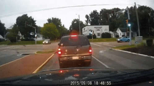 A Car Is Driving Down A Street With A Sign That Says Williams Plaza GIF
