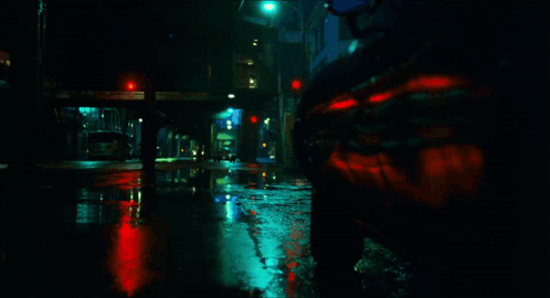 A Car Is Driving Down A Wet Street With A Red Light In The Background GIF
