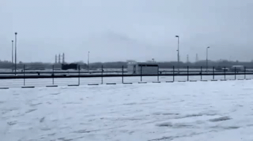 A Car Is Driving On A Snowy Road In A Parking Lot GIF
