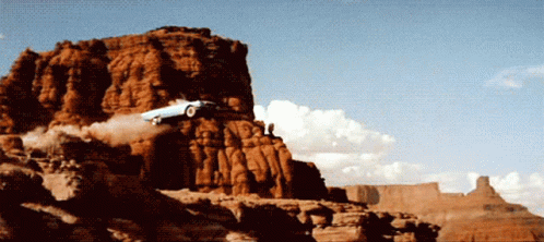 A Car Is Flying Through The Air On Top Of A Rocky Cliff GIF