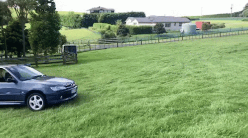 A Car Is Parked In A Grassy Field Next To A Fence . GIF