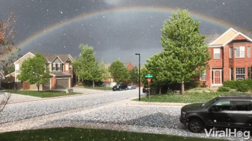A Car Is Parked In Front Of A Residential Street With A Rainbow In The Sky Above It GIF