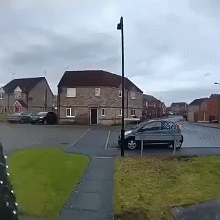 A Car Is Parked On The Side Of The Road In Front Of A Brick House GIF