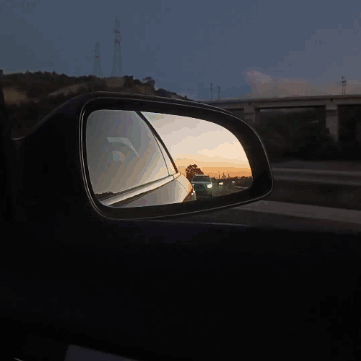 A Car Is Reflected In A Side View Mirror At Sunset GIF