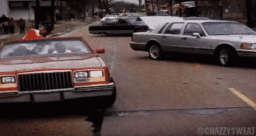 A Car With A Red Top Is Driving Down A Street Next To A Silver Car GIF