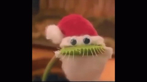 A Carnivorous Plant Wearing A Santa Hat With Googly Eyes . GIF